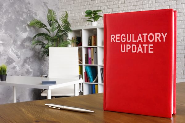 A red book standing on a wooden table showing the introduction of regulatory updates